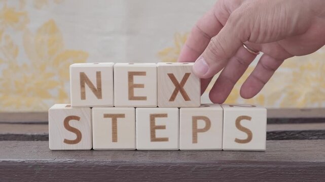 next steps, motivational phrase, laying out  by hand from letters on wooden cubes, slow motion
