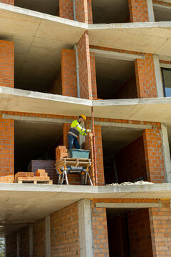 Professional builder checking alignment of red brick wall