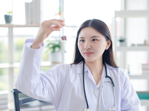 Asian young woman doctor holding look at test tubes red liquid of blood sample analysis medical vaccine innovation healthcare  scientist research technician development in laboratory hospital clinic.