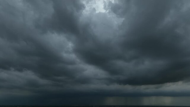Drone perspective of a powerful rainstorm system with dense dark clouds and visible rain falling from the sky, showcasing turbulent weather, atmospheric movement, the natural force of severe storms.
