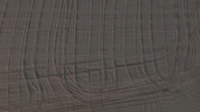 Cultivated farmland in the Po Valley near Cremona, Lombardy, Italy, revealing tractor tire tracks, tilled soil, agricultural field patterns and textured earth, top-down drone descent.
