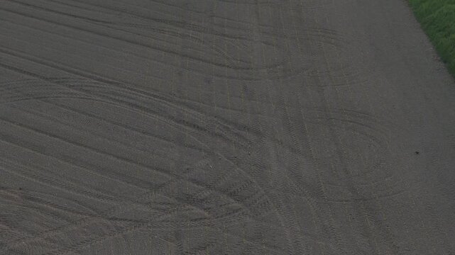 Cultivated farmland in the Po Valley near Cremona, Lombardy, Italy, revealing parallel tractor tracks, field edge, mature trees and textured tilled soil, top-down drone flyover.