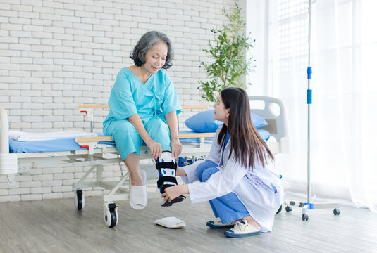 Asian woman healthcare professional fitting orthopedic walking boot on senior patient injured foot during rehabilitation in hospital medical care recovery physical therapy mobility support treatment.