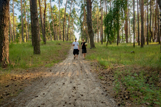 Two Teenage Friends Walking on a Sandy Path in a Sunny Pine Forest holding a Soccer Ball