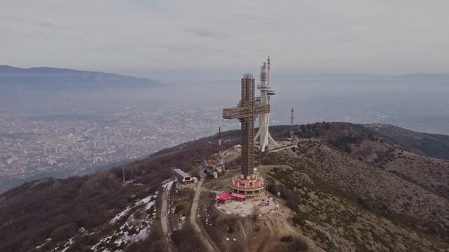 High angle aerial drone shot of Millennium Cross on Mount Vodno peak in Skopje North Macedonia with telecommunication tower and panoramic view of the capital city valley in the background.