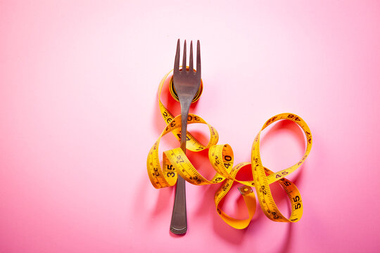 Fork and measuring tape on pink background. Dieting concept.