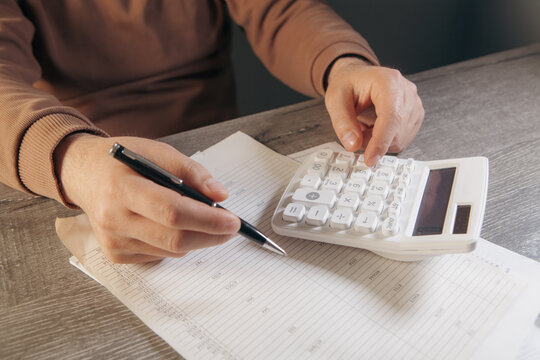 Man hand using calculator and writing in notebook on wooden table background.