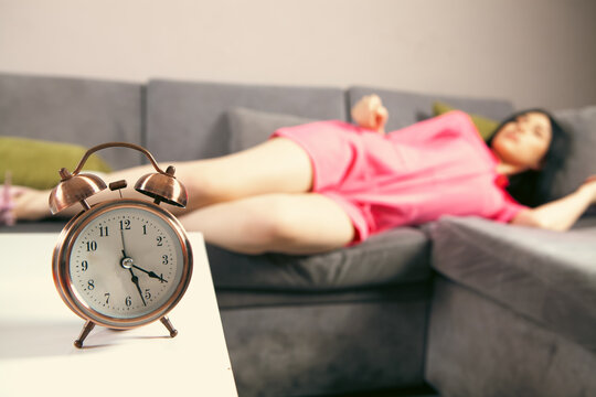Woman sleeping on sofa with alarm clock in foreground. Focus on alarm clock.