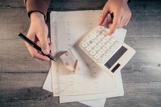 Man hand using calculator and writing in notebook on wooden table background.