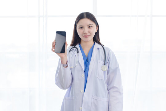 Portrait asian positive young woman doctor wearing white lab coat holding showing presenting screen mobile smartphone  in hospital clinic medical professional represents confident trust patient care.