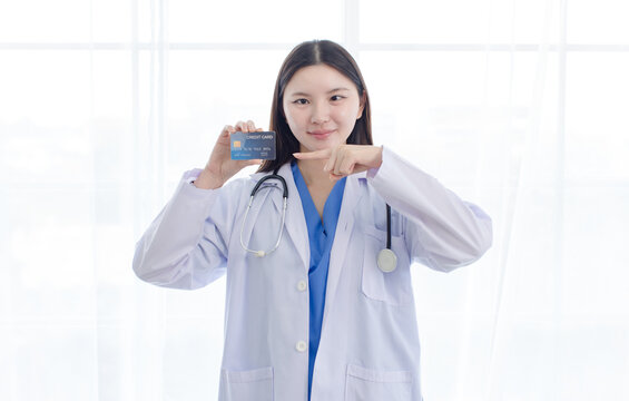 Portrait asian positive young woman doctor wearing white lab coat show holding presenting credit cards in hospital clinic medical professional lifestyle shopping online patient care health insurance.