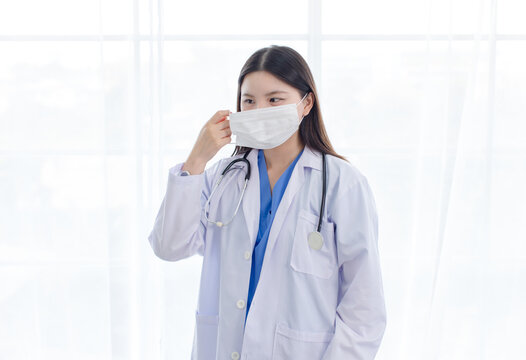 Asian woman doctor wearing protection face mask white medical coat in hospital clinic representing medical care infection flu disease prevention professional healthcare patient safety hygiene wellness
