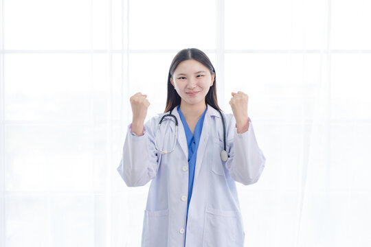 Portrait asian positive young woman doctor wearing white lab coat stethoscope standing happy raise arms excited for success in hospital clinic medical professional celebration confident patient care.