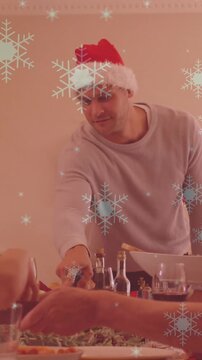 Animation of snow falling over smiling caucasian family with santa hats having dinner