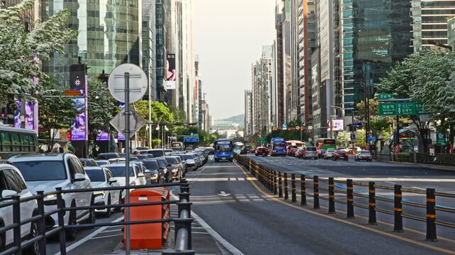 The busy streets of Gangnam feature wide, multi-lane avenues flanked by soaring modern glass skyscrapers, vibrant retail storefronts, digital displays, and steady urban traffic.