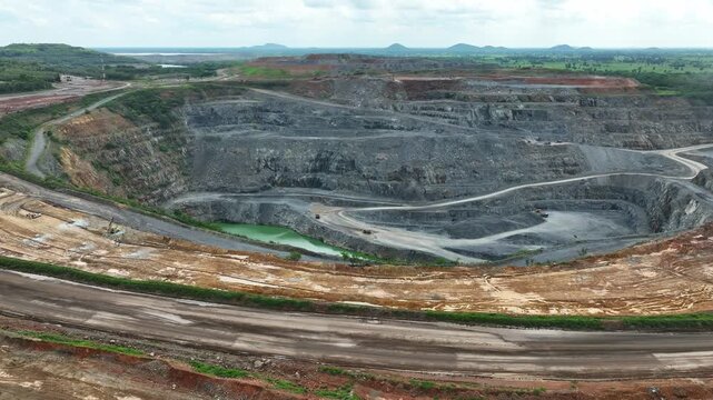 Aerial view of an active gold mine with terraced rock benches and heavy machinery, illustrating mineral extraction, industrial development, resource production, and large scale mining operations.
