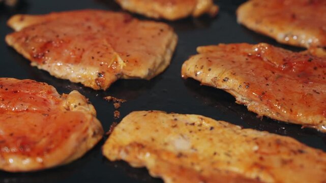Close-up tracking shot panning across seasoned chicken fillets cooking and browning on a hot flat-top commercial griddle.