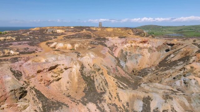 Parys Mountain Copper Mine, Amlwych, Anglesey, Wales, UK. Reverse drone flight away from derelict hilltop windmill revealing deep crater and mineral colours.