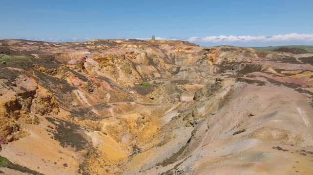 Parys Mountain Copper Mine, Amlwych, Anglesey, Wales, UK. Slow flight over main colourful deep crater towards distant derelict windmill.