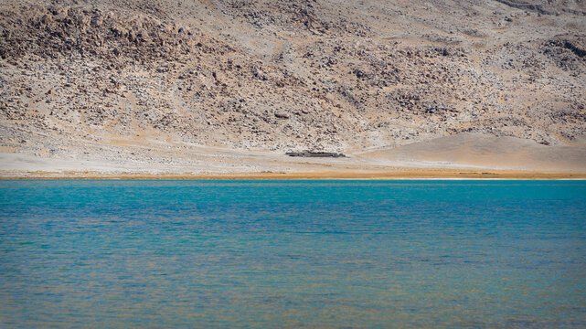 Minimalist view of turquoise alpine lake water with rocky mountain slope background in Eastern Pamir, Tajikistan
