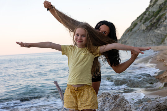 Smiling girl and mother playing together on a sandy beach by the sea, enjoying a fun summer day outdoors.