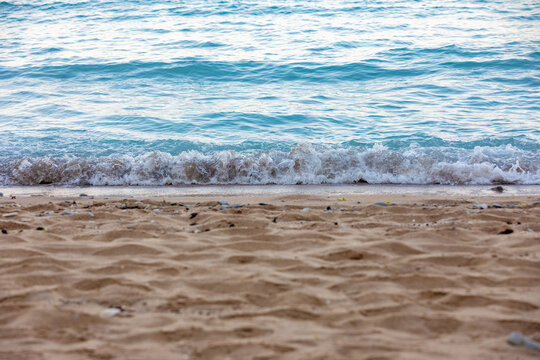 Close-up of gentle waves rolling onto a sandy beach with clear blue water, perfect for summer, relaxation, and travel themes.