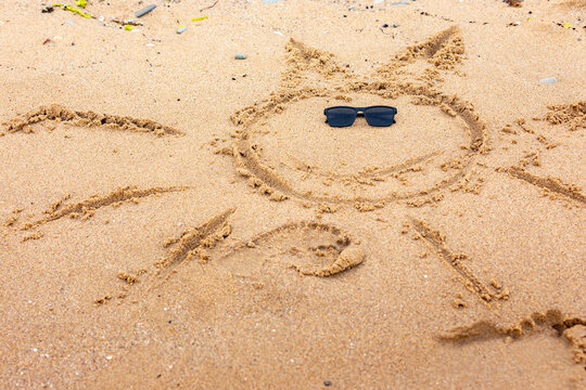Sun shape drawn in sand with sunglasses on a beach, representing summer, vacation, and fun outdoor relaxation.