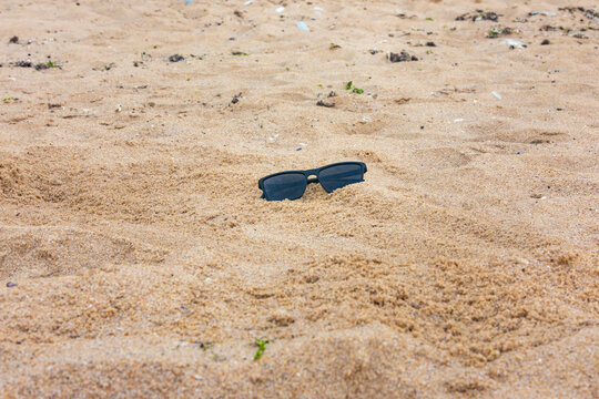 Black sunglasses partially buried in golden sand on a beach, evoking a relaxed, summer vacation mood. Ideal for travel, leisure, and lifestyle concepts.