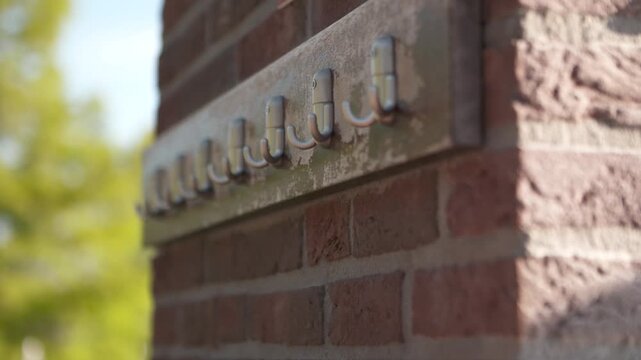 A hand hangs a pink robe on outdoor wall hooks against a sunny brick wall, capturing a relaxed everyday moment outdoors