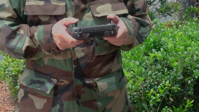 A soldier holds a drone controller while operating an unmanned aerial vehicle (UAV) during a military training exercise or combat support mission. The image represents modern battlefield technology, t