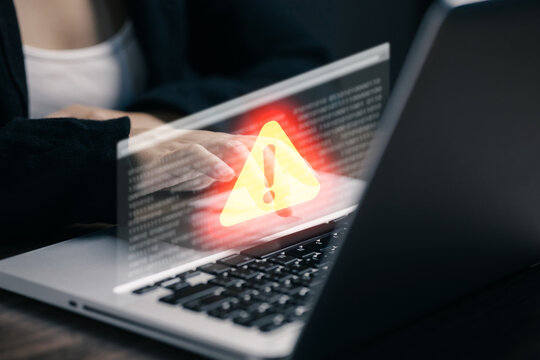 Business professional using laptop with glowing warning alert and code interface, illustrating cybersecurity risk, system error, malware threat, data breach, hacking, and online security.