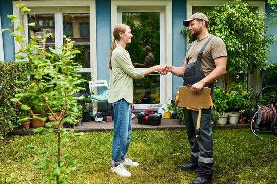 Caucasian female homeowner shaking hands with male technician in backyard, sealing deal for home maintenance services. Image suitable for local business marketing and home repair ads