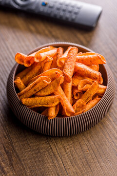 Spicy Corn Snack Chips in Bowl on Wooden Table With TV Remote for Movie Night