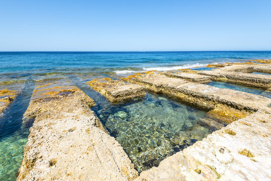 Wide-angle view of the historic Roman Baths in Sliema, Malta, showcasing natural limestone bathing pools filled with crystal-clear Mediterranean water along the island's scenic coastline.