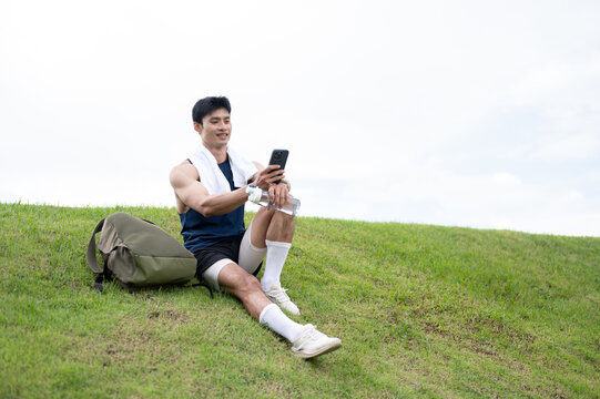 Athletic Asian Man Resting and Using Smartphone After Running