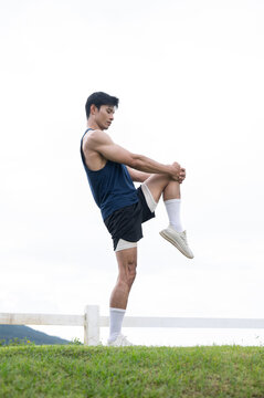 Athletic Asian Man Stretching Knee After Running