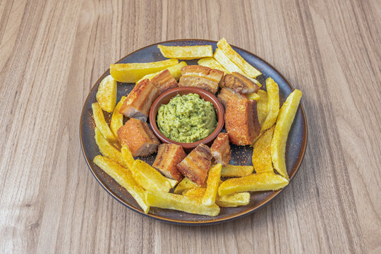 Roasted Pork Belly Chunks Encircled by Seasoned Fries with Green Herb Sauce on Plate