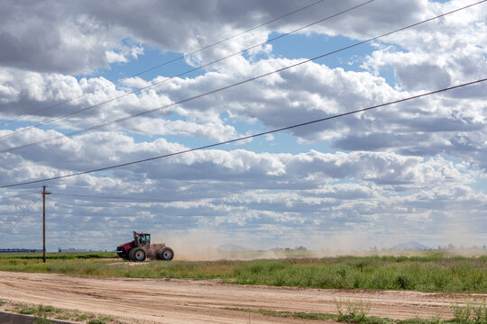 Red tractor kicking up dust in a rural field