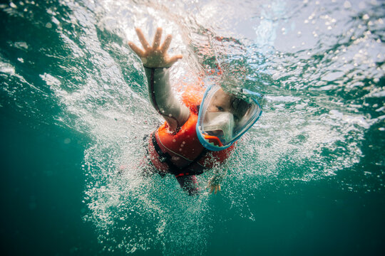 Young kid in snorkel mask waves from underwater