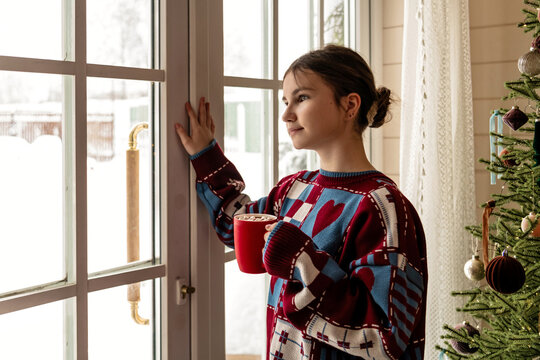Teenager with hot cocoa looking out a snowy window