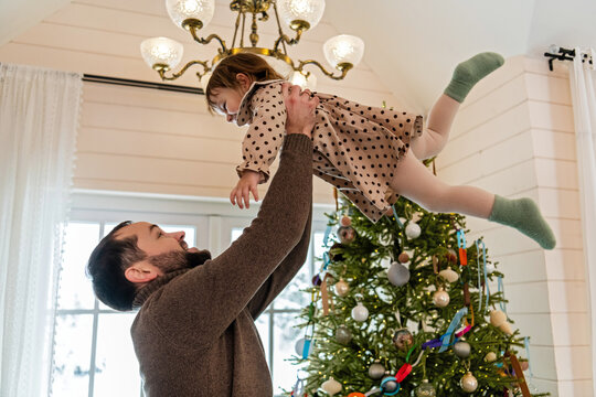 Playful dad tossing toddler girl near Christmas tree