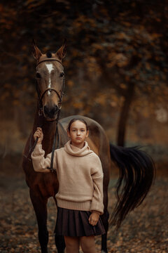 A young girl with a brown horse outdoors in an autumn forest