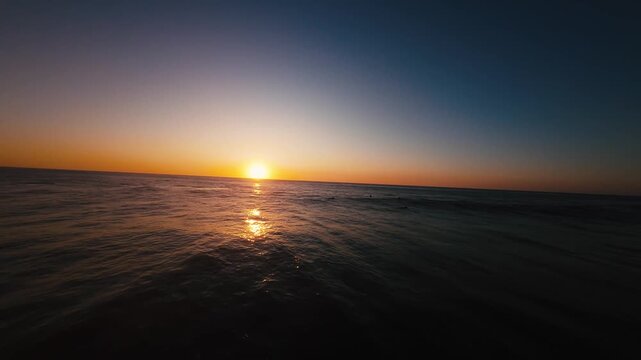 Sun dips low, painting ocean in molten gold. Wave crashes softly, foam glows warmly. Sky shifts from deep blue to rich amber. Silent, peaceful, golden hour over water. Perfect for serene travel