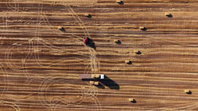 Aerial view of loader loading straw bales onto truck in field at sunset