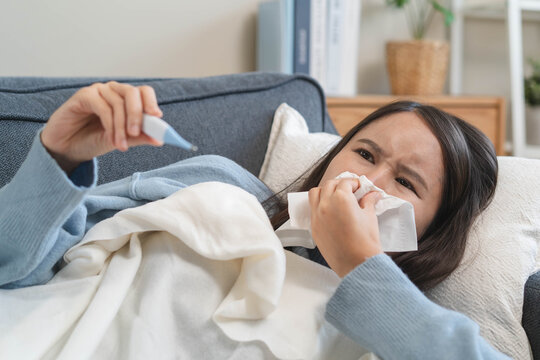 Sick person resting in bed checking temperature with thermometer, suffering from high fever, seasonal flu, influenza virus infection, and common cold symptoms at home