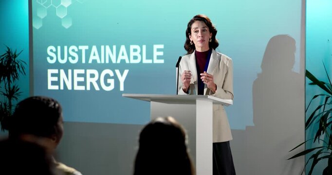 Woman, presentation and podium with speech for sustainable energy or eco friendly campaign launch. Female person, speaker or environmentalist talking with crowd in seminar for natural business growth