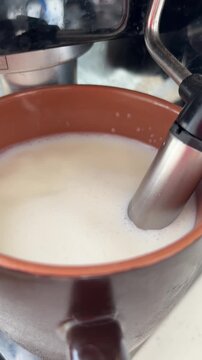 Barista frothing milk with an espresso machine steam wand for making cappuccino, a detailed close up shot showing the preparation of hot coffee with white foam