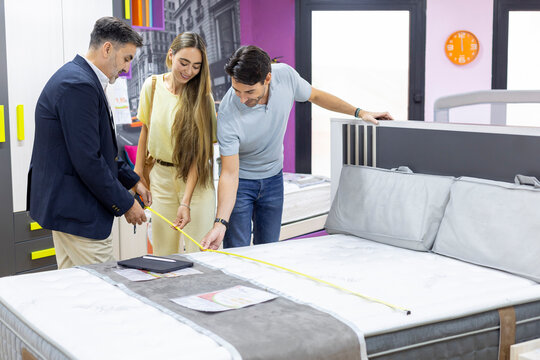 Sales assistant helping couple measuring mattress dimensions