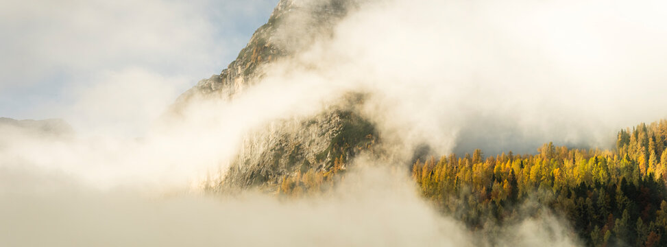Scenic mountain landscape with mists obscuring autumn larch trees, capturing the spirit of nature adventure and tourism exploration near Sella Nevea, Julian Alps, Chiusaforte, Friuli, Italy.