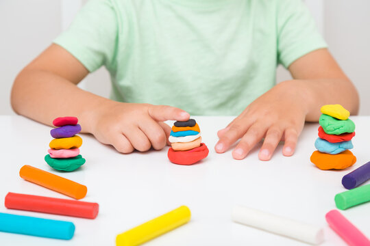 Little boy hands making and creating towers from colorful modeling clay on white table at home room. Closeup. Little child handcraft. Front view.